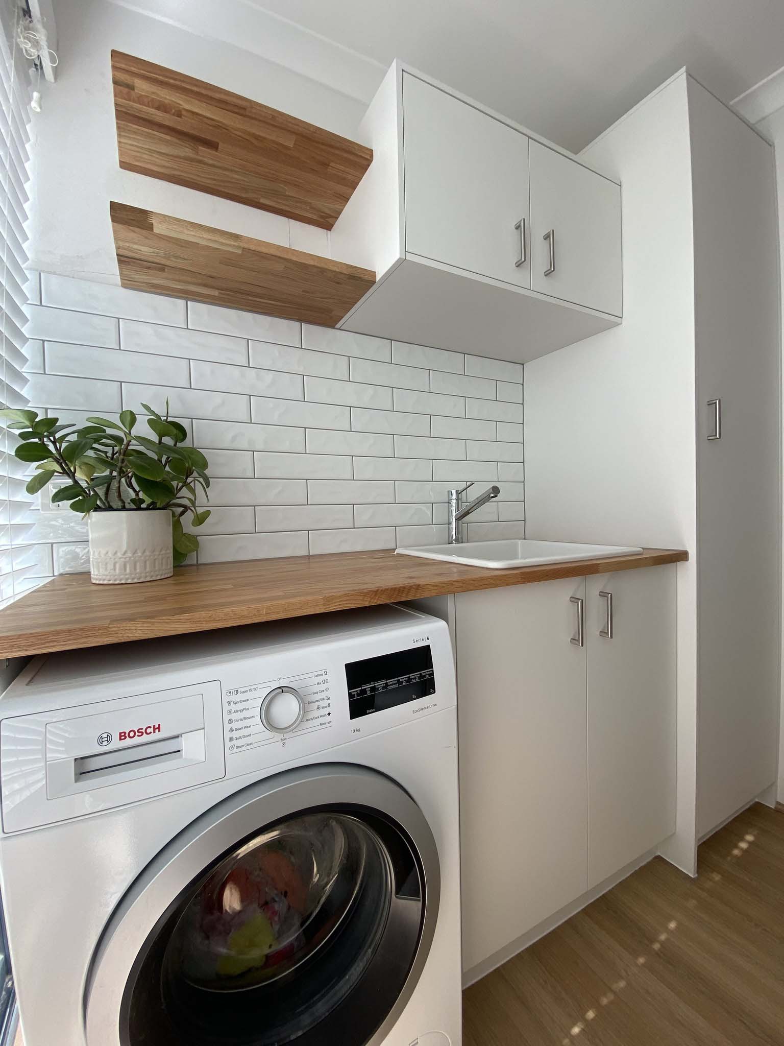 1b-home-about1 Laundry with white cabinets, timber benchtop, floating shelves and a front-loader