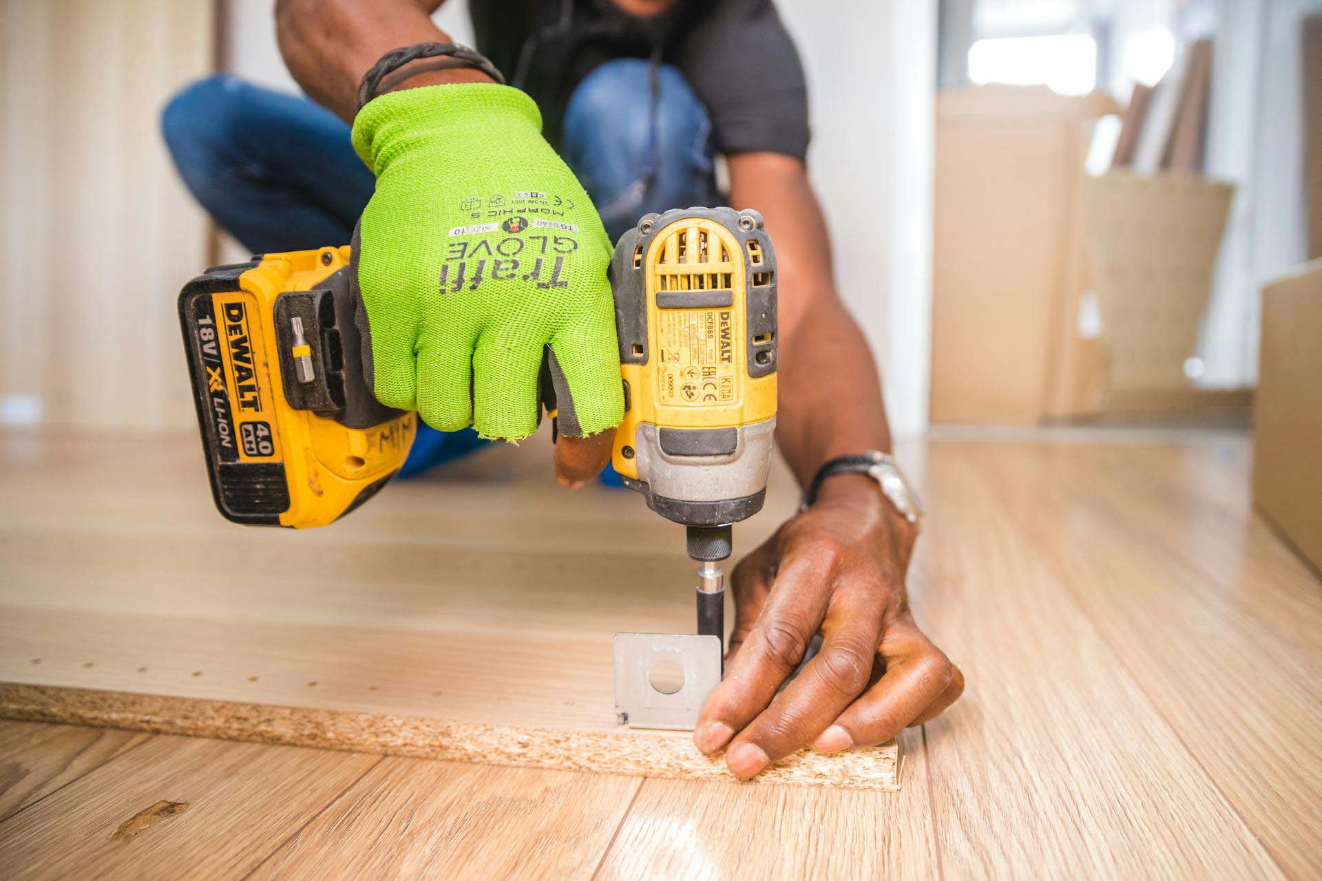 1c-home-give-back Gloved hands driving a screw into a chipboard panel with a cordless drill